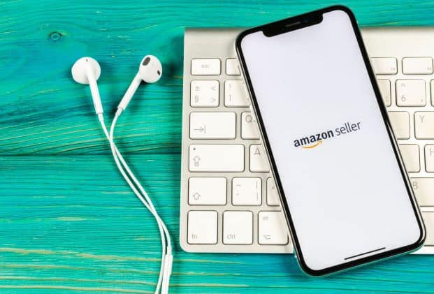 A phone with the Amazon logo on it next to a keyboard and earphones designed for marketplace sellers.