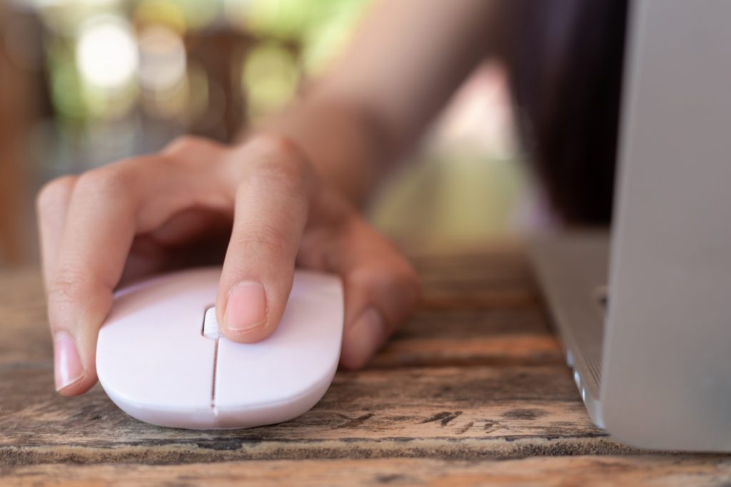 A woman is using a computer mouse on a wooden table while shopping on an online marketplace.