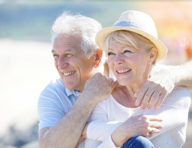 An older couple embracing each other warmly on the beach.